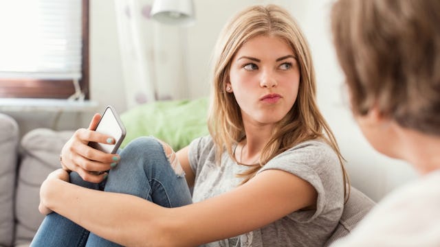 A blonde teen girl wearing a gray shirt and jeans with an angry face while her mother is trying to m...