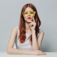A woman sitting in a white top and yellow glasses and she looks angry because of other people being ...