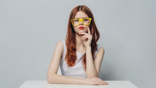 A woman sitting in a white top and yellow glasses and she looks angry because of other people being ...