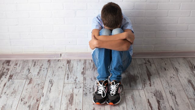 A sad boy with ASD sitting alone on the floor in an empty room