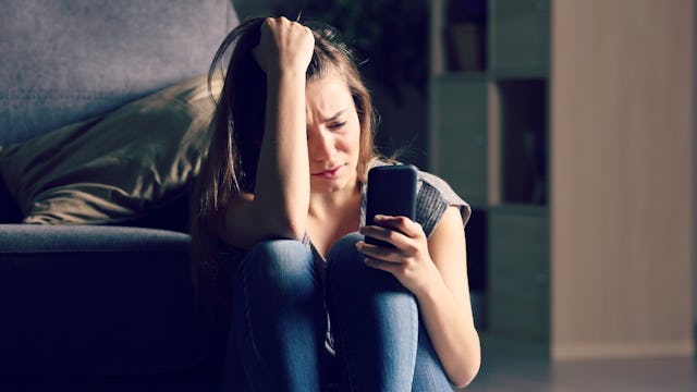 A woman with brown hair who loves ab alcoholic spouse, crying and looking at her phone 