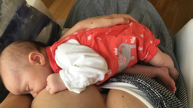 Mélanie Berliet's baby breastfeeding in peach overalls and a white shirt 