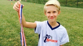 A young blond boy holding his medal from a football match 