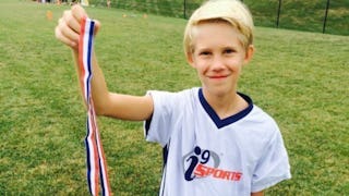 A young blond boy holding his medal from a football match 