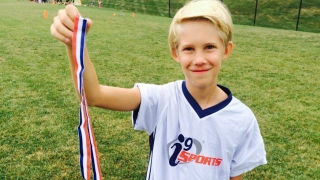 A young blond boy holding his medal from a football match