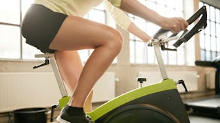 A closeup of a girl training on an indoor cycling bike in the gym while wearing matching black short...