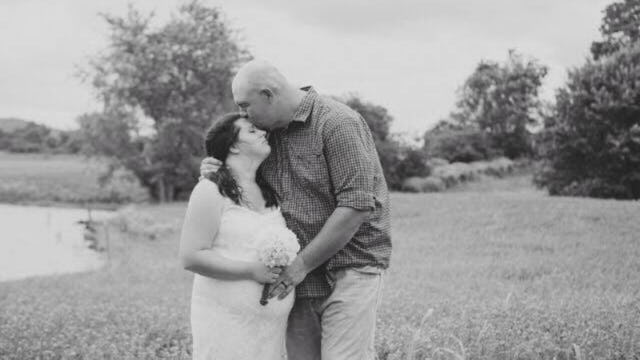 A pregnant lady standing in a wedding dress next to a man who is kissing her forehead