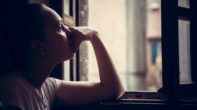 A woman leaning her chin on her hand while looking through a window after the loss of her mother.