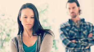 A sad black-haired woman with a man behind looking at her