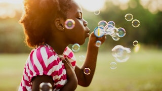 The profile view of a curly-haired kid in a pink-white striped T-shirt blowing bubbles