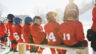 A kid's hockey team dressed in red hockey gear, sitting on a bench waiting for the game