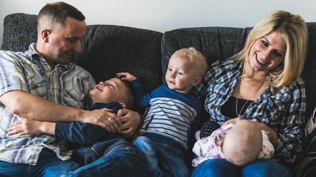 Parents happily sitting on the couch while playing with their three kids in their home