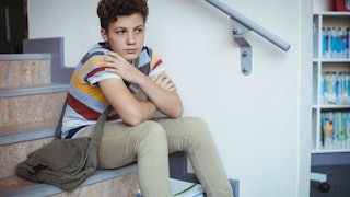 A middle schooler sitting on stairs looking like he is struggling with something