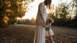 A child hugging her second-time pregnant mother.