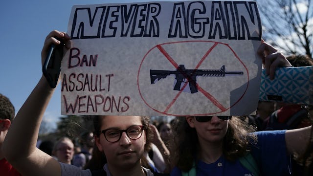 Two women with glasses holding a poster with a message about banning assault weapons amid a #NeverAg...