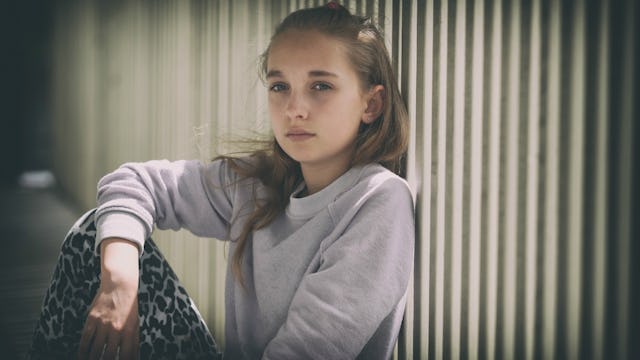 A mad and aggressive looking girl sitting leaned against a school fence