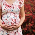 A woman in a floral dress hugging her pregnancy belly.