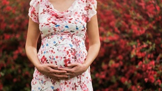 A pregnant woman in a floral dress hugging her belly.