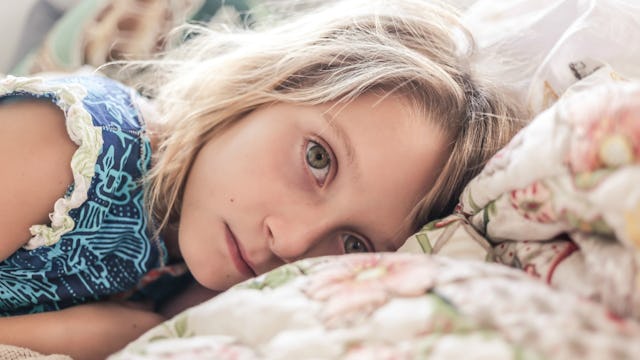 A blonde girl in a blue shirt lying stomach down with a neutral facial expression, whose sensitivity...