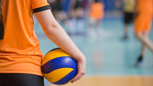 A girl in an orange jersey and black shorts holding a volleyball ball.