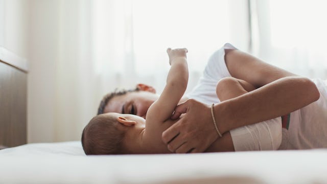A single mom in a white shirt and a newborn child playing on a bed