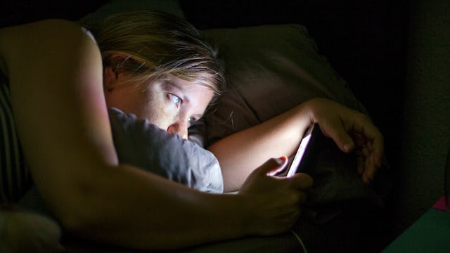 A mother scrolling through social media in a dark room during the night