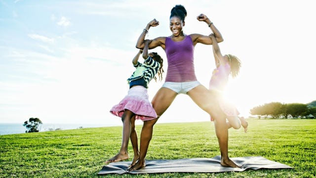 A woman in a purple tank top and white shorts is showing off her biceps while two kids are clinging ...