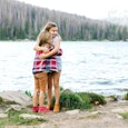 A mother is photographing her two daughters hugging for a social media post each other next to a lak...