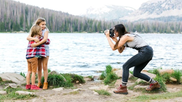 A mother taking a photo of her two daughters hugging for a social media post, each other next to a l...