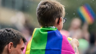 A small kid wearing a rainbow flag over his back representing a trans-kids trend 