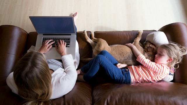 A working mom using her laptop while her daughter is sitting next to her on a brown leather couch