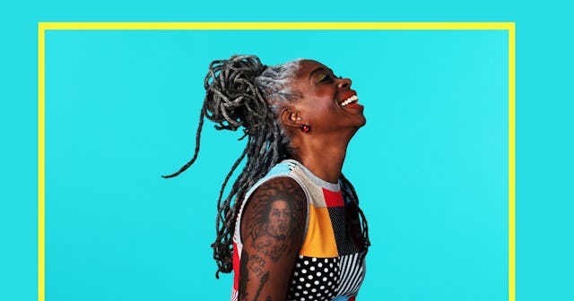 The profile of a laughing woman with dreadlocks, arm tattoos, and a sleeveless color-block top