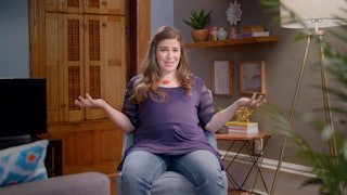 A 34-week pregnant woman with her arms spread out talking about how she's just over it 