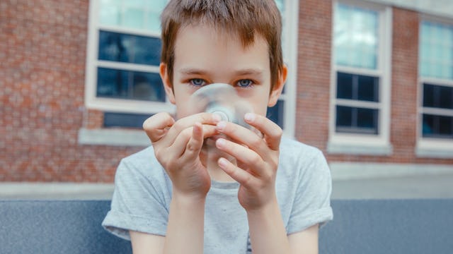 A brown-haired boy with autism, wearing a grey T-shirt spinning a fidget-spinner in front of his fac...