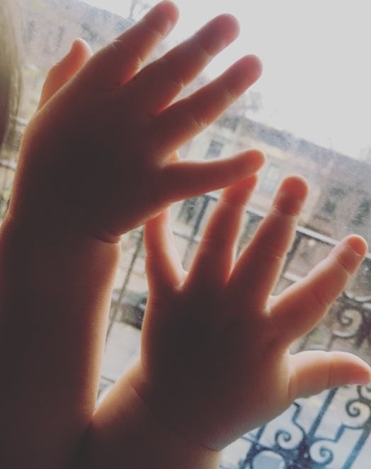 Two baby hands leaning against a window 