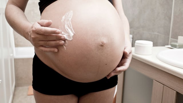 A pregnant woman putting shaving cream on her stomach 