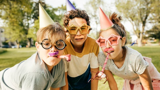 Three kids wearing birthday hats and party blowers in a park