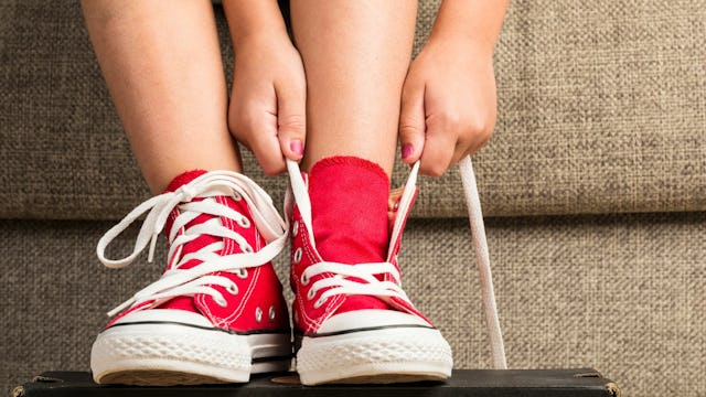 A kid with painted nails tying red All Star shoes