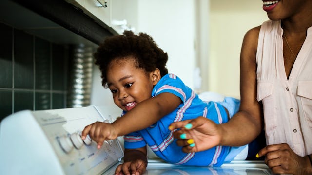 A stay-at-home mom in a beige sleeveless shirt playing with her child in a blue shirt around a washi...