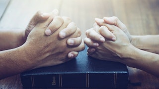 Two Christians praying with their hands on the Bible 