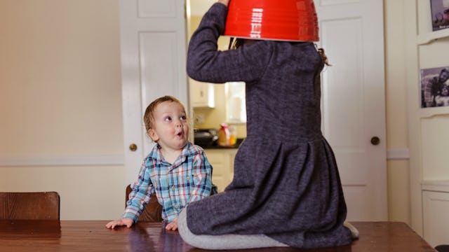 Two kids playing on a brown kitchen table; the boy is in a blue checked shirt and the girl is in a g...