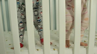 Two babies wearing pajamas, standing in a white baby crib