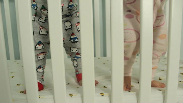 Two babies wearing pajamas, standing in a white baby crib