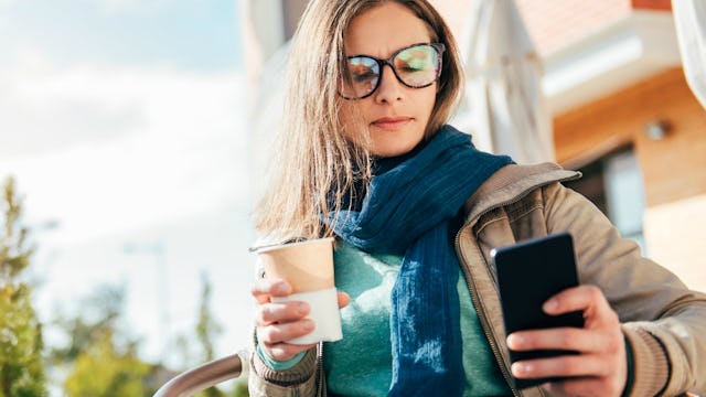 A woman texting her friend on the phone while drinking coffee