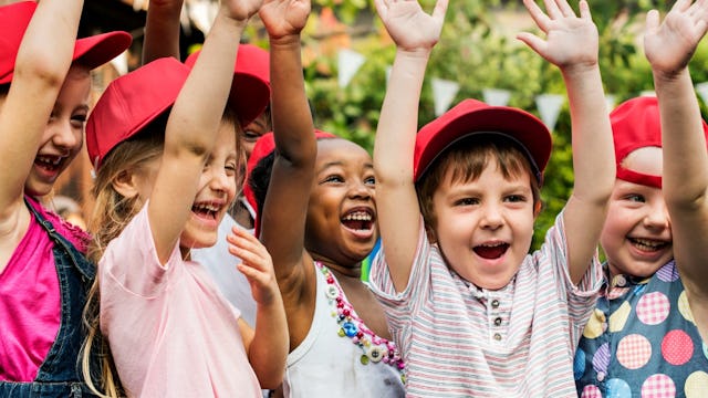 A group of children wearing red caps, laughing with their hands in the air at the daycare.