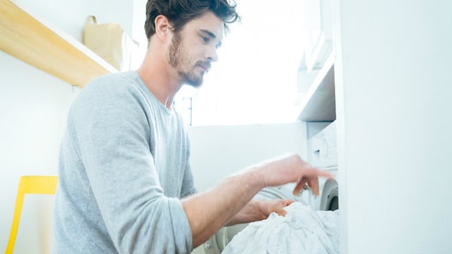 A man with black hair loading laundry in the washer