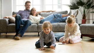 Parents resting on the couch while their daughter is drawing, and a younger son is crawling in front...