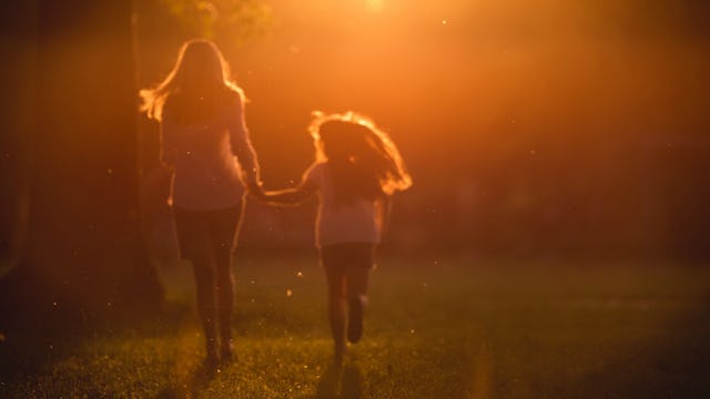 A mother and daughter holding hands and running across a field