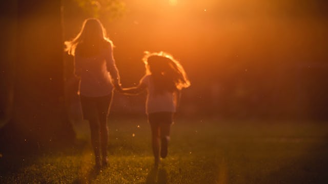 A mother and daughter holding hands and running across a field 