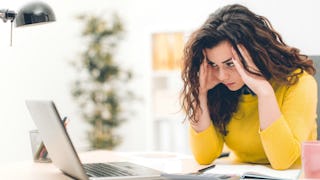 Young girl with an annoyed face sitting in front of her laptop, wearing a yellow shirt